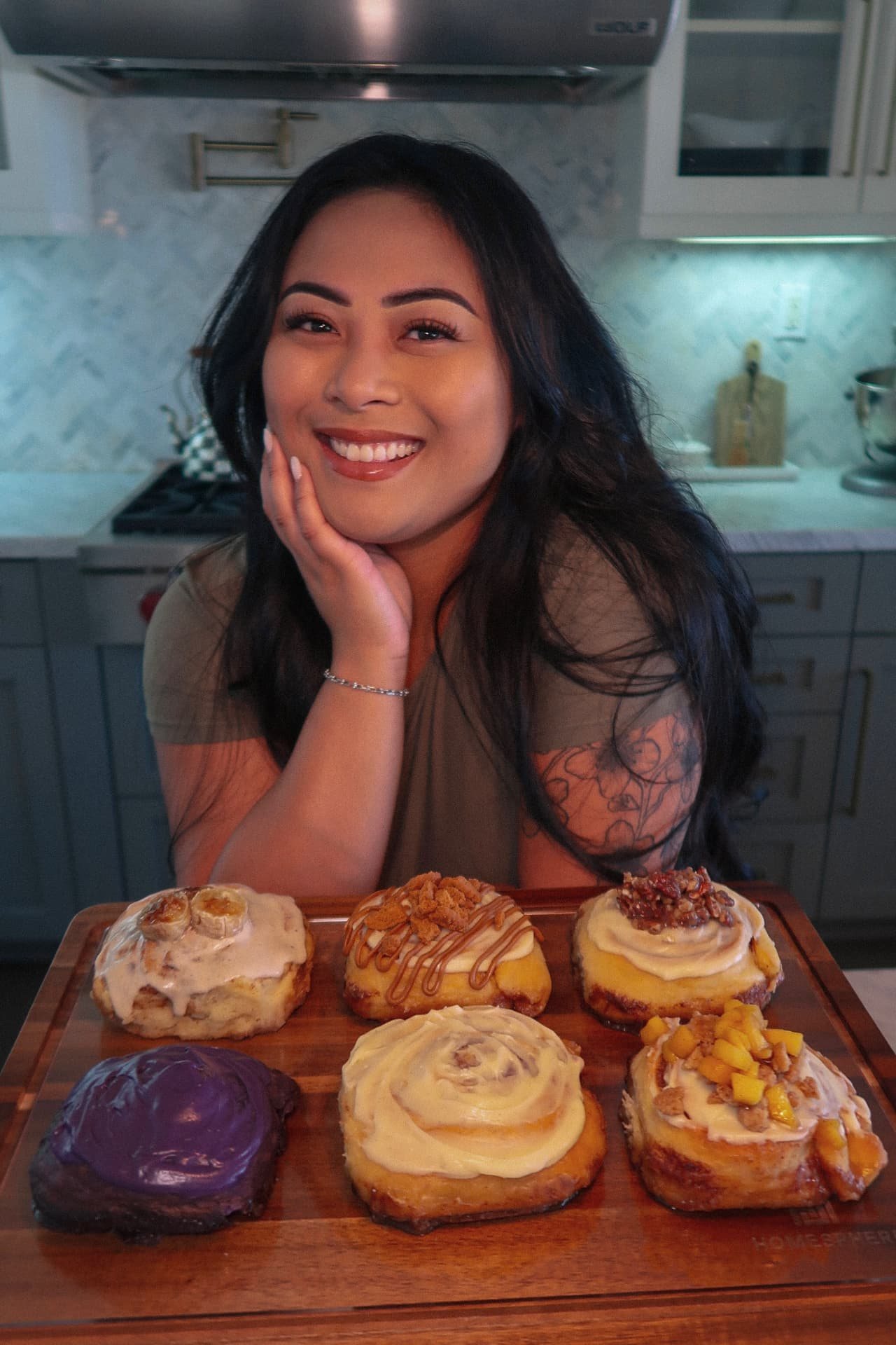 Jessica behind her kitchen counter with a board of fresh cinnamon rolls