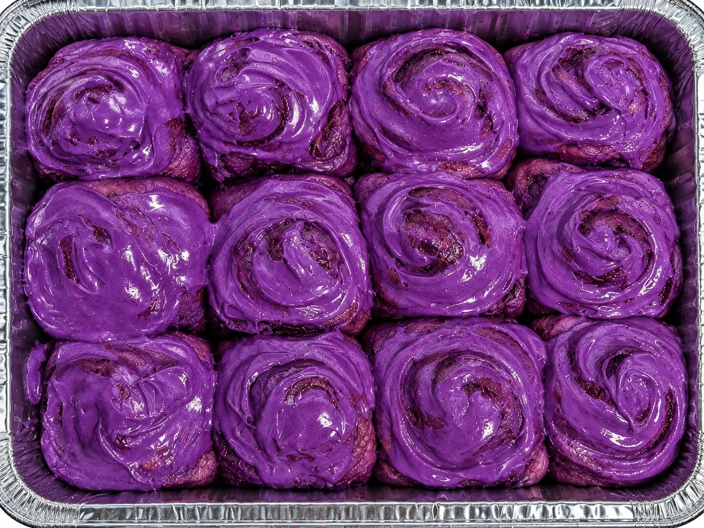 A pan of ube cinnamon rolls finished with a glossy purple ube glaze